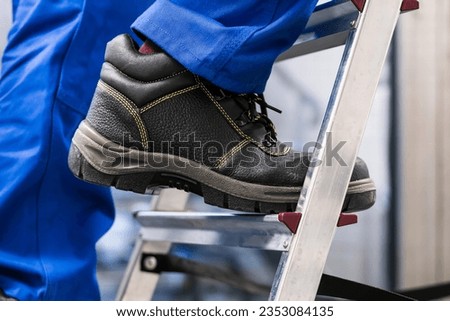 Low Section View Of A Handyman's Foot Climbing Ladder Royalty-Free Stock Photo #2353084135