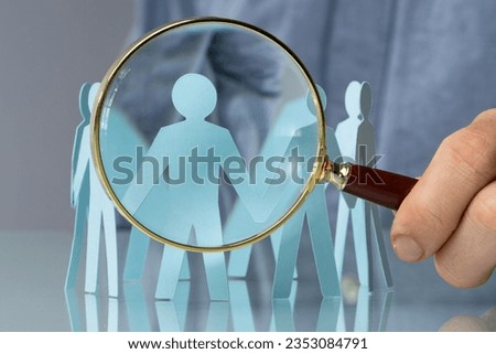Holding Magnifying Glass And Paper People. Closeup Shot