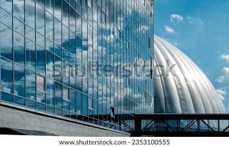 The wall of the building is made of glass and concrete with a reflection of the sky.