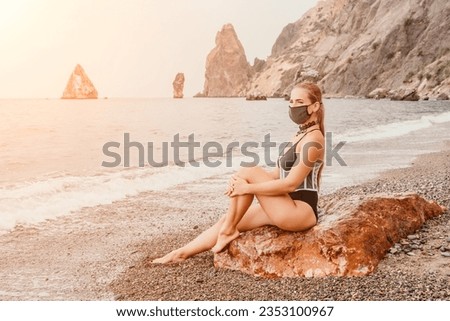Woman travel portrait. Happy woman with long hair poses on a red volcanic rock at the beach. Close up portrait cute woman in black bikini, smiles at the camera, with the sea in the background.