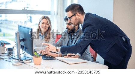 Male executive businessman showing important data on computer screen to his colleague while they are gathered around desk in the office. Royalty-Free Stock Photo #2353143795
