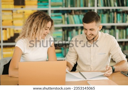 Portrait of boy and girl study in public library. Female using laptop and boy write something in notebook 