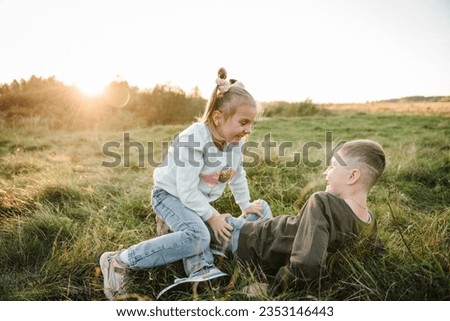 Kids playing in mountains on autumn day. Daughter, son hugs lying in green grass in field at sunset. Happy children walking spending time together in nature. Family holiday. Portrait child in summer.