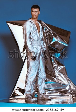 Holographic, vaporwave fashion and man with futuristic ski style with sci fi clothing in studio. Art, creative and male model with trendy, cool and cyberpunk designer clothes with blue background