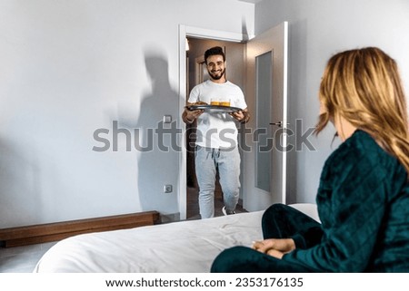 The husband of a young couple brings him the breakfast he has prepared for his wife who is waiting for him in bed. Husband prepares a surprise for his wife. Romantic breakfast. Domestic lifestyle.
