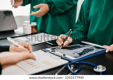 Medical team having a meeting with doctors in white lab coats and surgical scrubs seated at a table discussing a patients working online using computers in the medical industry
