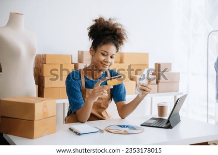 Young woman holding a smartphone, tablet showing payment success and credit card with yellow parcel box as online shopping concept in office Royalty-Free Stock Photo #2353178015