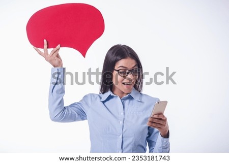 Beautiful young business lady in classic shirt and eyeglasses is holding speech bubble, using smart phone and smiling, isolated on white