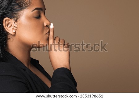 Keep silence. Latin woman showing shh gesture, mysterious lady holding finger near lips, gesturing hush while standing over brown background, side view, copy space Royalty-Free Stock Photo #2353198651