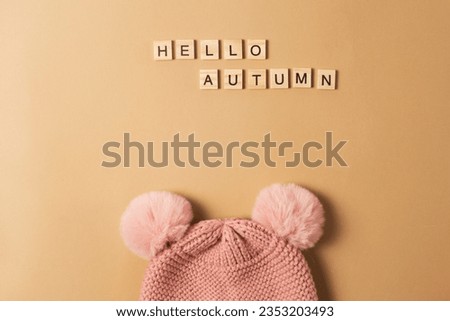 Pink knitted hat with pumpons on a brown background with the inscription hello autumn