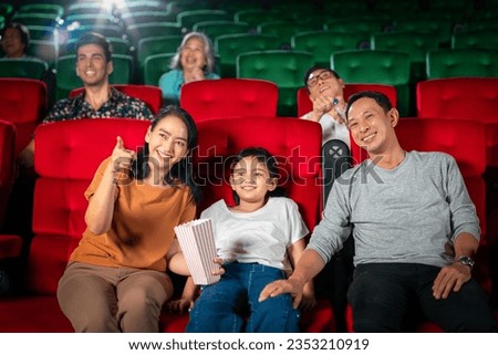 Happy trip of asian family sit togather on red seat and looking  movie in cinema with fun a popcorn on hand, people relax and holiday activity on a weekend