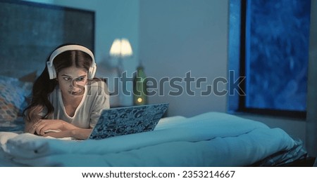 Frightened Indian young woman  lying on bed watching horror scary movie at indoor home. Beautiful scared girl using headphones looking fearful film on laptop webcam screen enjoying late night alone Royalty-Free Stock Photo #2353214667