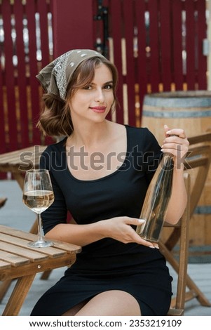 Beautiful young woman drinking white wine on the terrace of a restaurant. The attractive woman is holding a bottle of white wine. picture for wine advertising