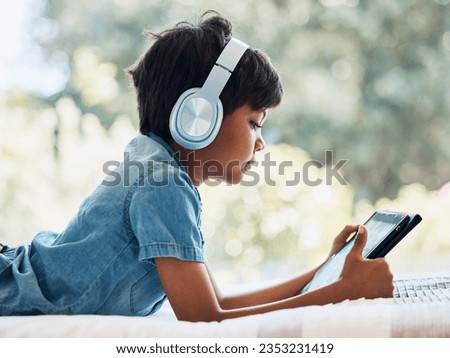 Boy child, tablet and headphones on bed, reading or idea with e learninng, movie and web video to relax. Male child, digital touchscreen and thinking in bedroom for games, music and streaming in home