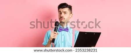 Holidays concept. Funny man with bow-tie making speech, perform on party events, holding script on clipboard and microphone, entertaining you, standing over pink background.