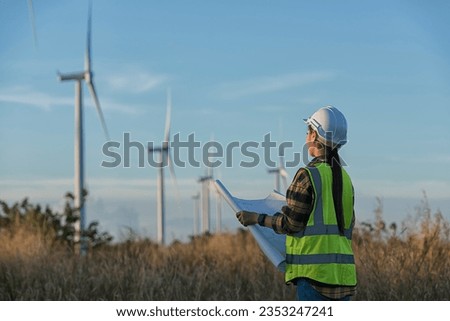  Woman engineers with drawing against turbines on wind turbine farm. Royalty-Free Stock Photo #2353247241