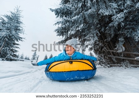 Child races down snowy slope on tubing. Inflatable sleds for active winter recreation. Beautiful snowy winter forest background.