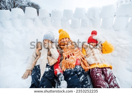Three children are playing in snow fort made of ice blocks. Wide angle shooting. Active winter outdoor games. Warm winter clothes for children.