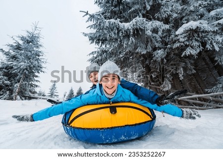 Smiling children ride down on inflatable tubing sleds. Inflatable sleds for active winter family recreation. Beautiful snowy winter forest background.