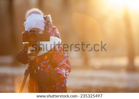 Pretty girl photographer taking pictures on camera using a tripod, sunset light, winter, copyspace