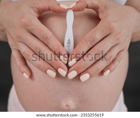 Caucasian woman holding a positive express pregnancy test against the background of her tummy. 