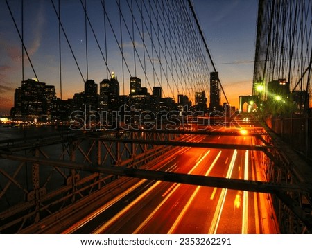 A long exposure photo of the Brooklyn Bridge at night, with the Manhattan skyline in the background. Light trails visible.