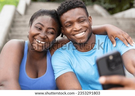 Young smiling friends hugging holding mobile phone watching video, taking selfie, communication online on the street. Happy African American man and woman recording video with smartphone. Technology 