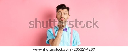 Cute boy sending air kiss at camera and saying I love you on Valentines day, standing over romantic pink background in bow-tie and shirt.