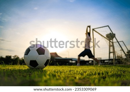 Action picture of sport player playing soccer football for exercise at green grass field park under the sunset. Picture with copy space.