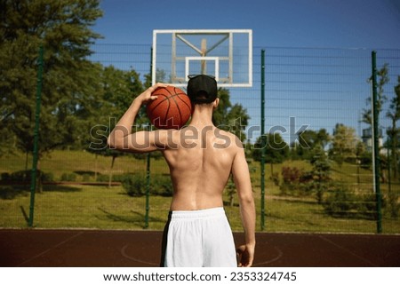 View from back of muscular basketball player holding ball on shoulder