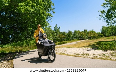 Mother and her Girl having a ride on road with electric cargo bike at summer.