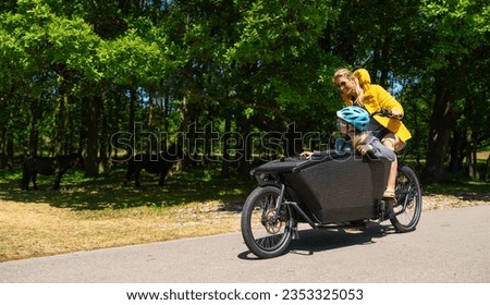 Happy Mother and daughter having a ride on road with electric cargo bike in nature