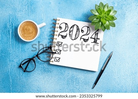 New year resolutions 2024 on desk. 2024 goals list with notebook, coffee cup, plant on blue table. New Year 2024 resolutions. Resolutions, plan, goals, action, checklist, idea concept. Copy space