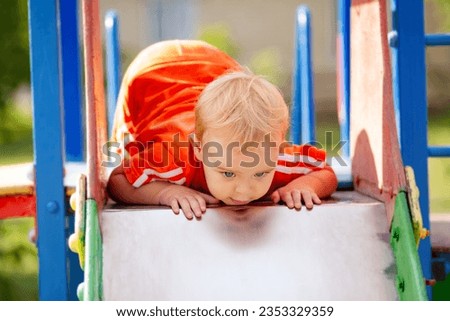 Cute little boy walking in park, child climbed onto the slide on playground to move down, leisure activity concept