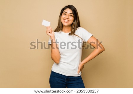 Latin young woman wearing a white mock-up t-shirt with copy space holding a credit card for shopping Royalty-Free Stock Photo #2353330257
