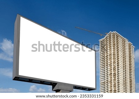 A large information display for advertising on the street in the city, against the backdrop construction of a skyscraper and a beautiful sky.