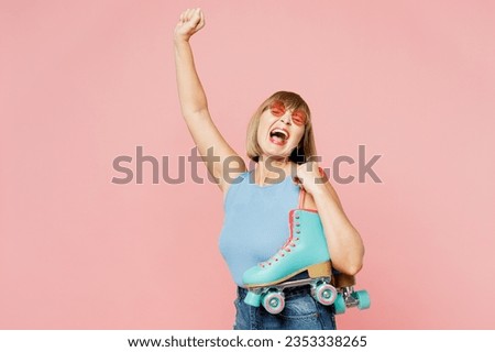 Overjoyed elderly blonde woman 50s years old she wearing blue undershirt casual clothes do winner gesture hold roller bladers isolated on plain pastel light pink background studio. Lifestyle concept