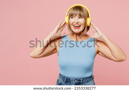 Elderly blonde woman 50s years old she wears blue undershirt casual clothes listen to music on headphones look aside on area isolated on plain pastel light pink background studio. Lifestyle concept