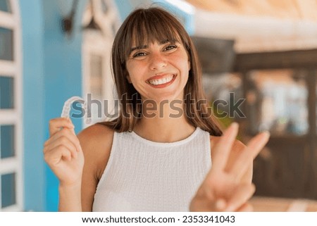 Young woman holding invisible braces at outdoors smiling and showing victory sign