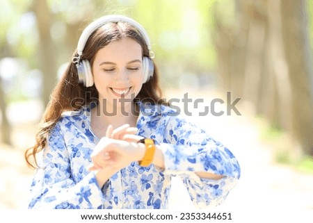 Happy woman with headphone checking smartwatch in a park