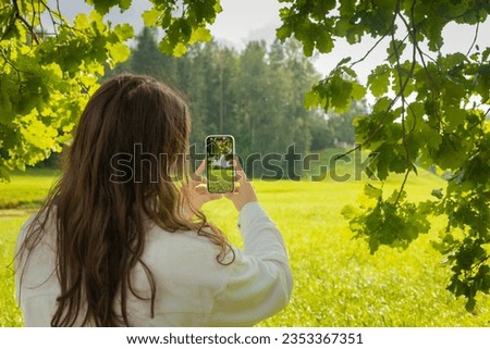 a young woman holds a smartphone in her hands and takes pictures of a beautiful natural landscape in the forest in summer