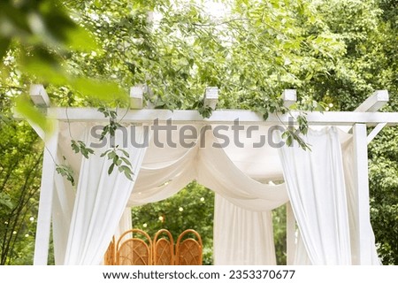 Bungalow with roof with light curtains in garden. Summer gazebo with flowing white curtains for relax outdoor. Wedding decorations. Romantic alcove with baldachin. Decor outdoor terrace with canopy.   Royalty-Free Stock Photo #2353370677