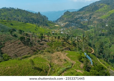 Hilly landscape of Sri Lanka dotted with villages and tea plantations viewed from a train.