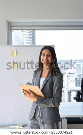 Confident happy professional young Indian business woman company employee, lady executive manager, smiling female worker looking at camera standing in modern office with whiteboard, vertical portrait.