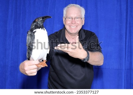 Photo Booth. Penguin. Pet Penguin. A man poses and smiles with his Penguin while having his picture taken in a Photo Booth. Penguins Love Photo Booths. Take your Pet Penguin to work. Crazy and Funny. 