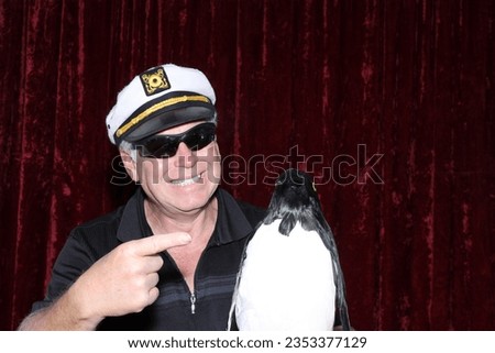 Photo Booth. Penguin. Pet Penguin. A man poses and smiles with his Penguin while having his picture taken in a Photo Booth. Penguins Love Photo Booths. Take your Pet Penguin to work. Crazy and Funny. 