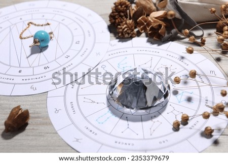 Astrology prediction. Zodiac wheels, pendulum, gemstone and dry flowers on wooden table, closeup