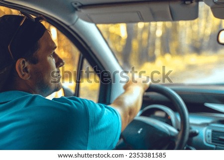 Portrait. Handsome man driving a car looks in the rearview mirror while traveling. A nice man is traveling in his car around the country. Concept of a male traveler driving a car.