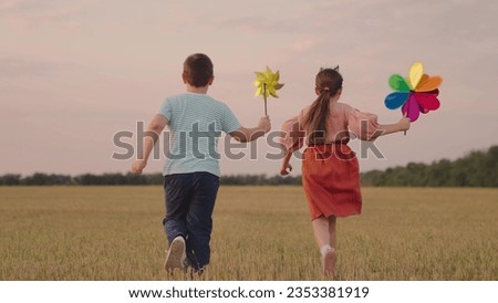 Childrens play pinwheel in nature. Happy children play with toy pinwheel outdoors in summer on field, running in park. Boy girl play together, wind turns circle toy. Family vacation in nature. Kid fly Royalty-Free Stock Photo #2353381919