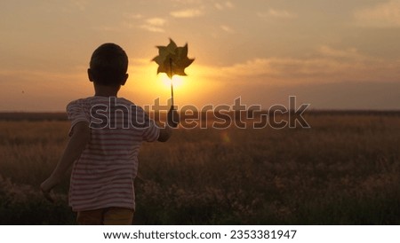 Active kid plays with toy pinwheel outdoors in spring park in sunshine. Childhood, children. Little boy runs with toy wind turbine in his hand on summer field at sunset. Family vacation in nature, sky Royalty-Free Stock Photo #2353381947